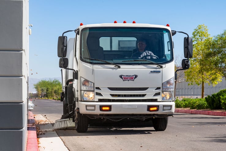 A close up view of a trucker sweeper sweeping a roadside curb