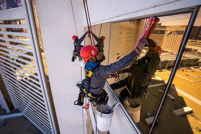 Property services professional using an atrium lift to clean high rise windows of a tall building